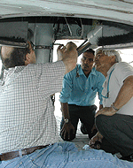 This is a photo. (From left) Richard Denson, Maldivian technician Ishag Abdulla, Al Montes and Maldivian engineer Ibrahim Imran repair the landing gear on the FAA Challenger jet.